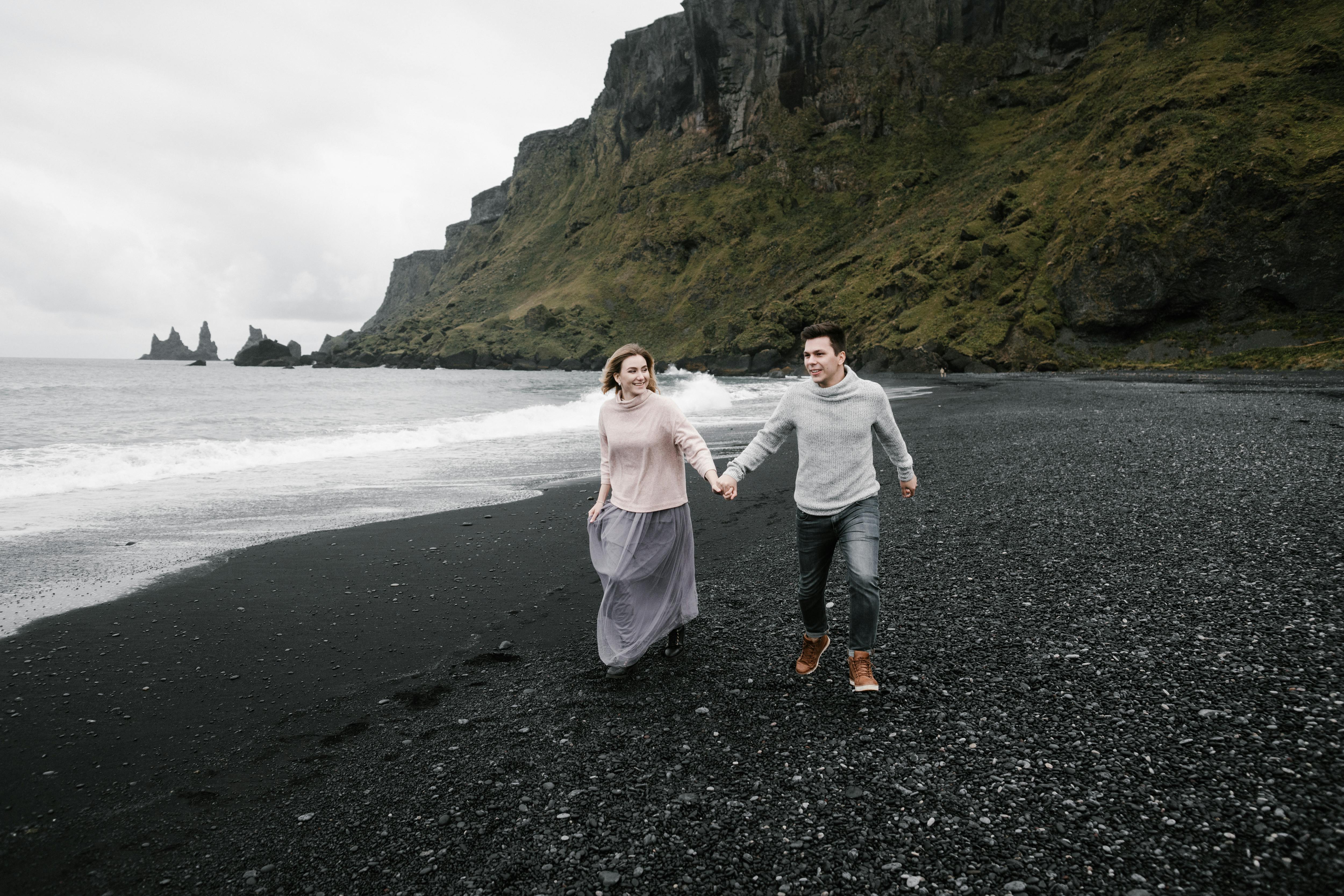 An image of a couple running on a black sand beach in iceland.